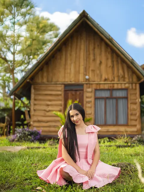 Kenia sentada en el jardín frente a la cabaña, con vestido rosa